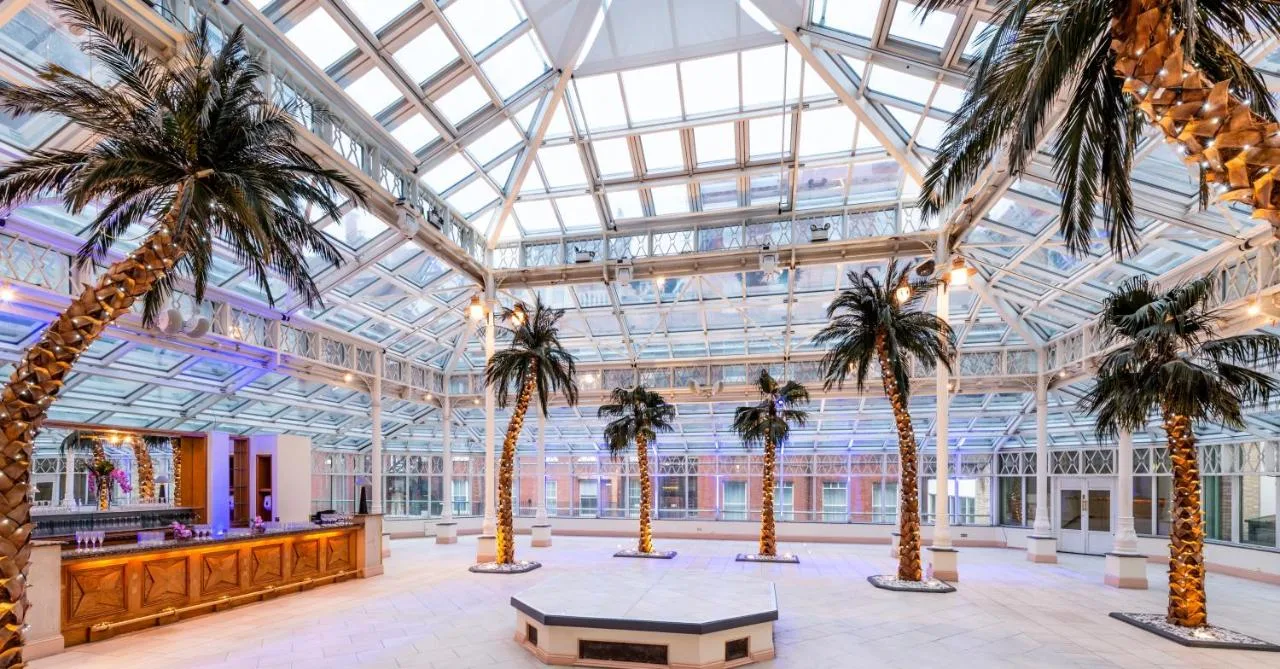a lobby with palm trees and a glass ceiling at Millennium Hotel and Conference Centre Gloucester London in London